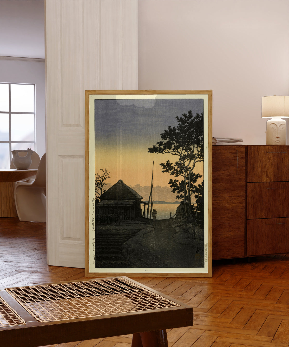 Framed art print of Dusk at Aso, Ibaraki by Kawase Hasui, in a light wood frame leaning in a warm room with a parquet floor