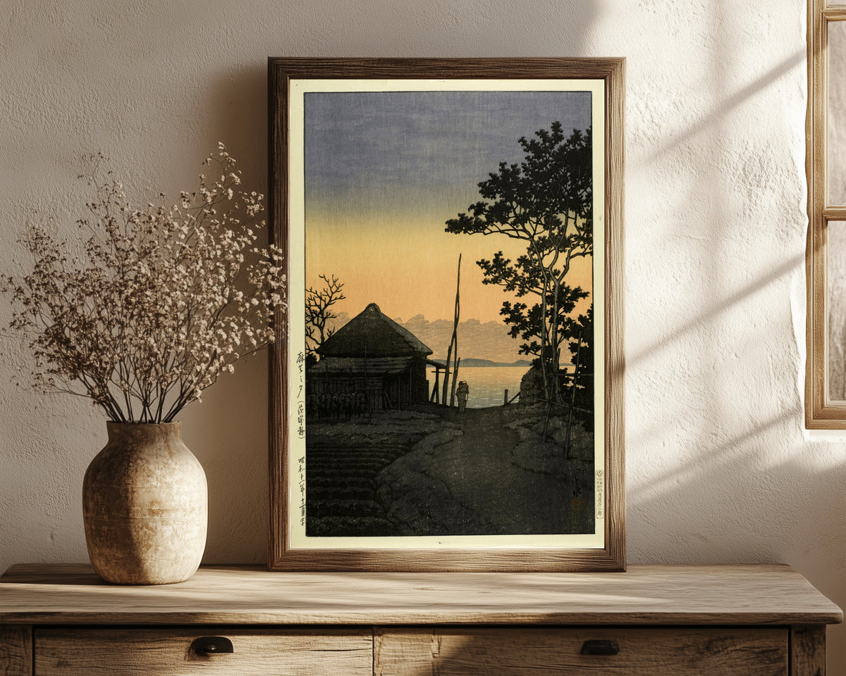 Framed art print of Dusk at Aso, Ibaraki by Kawase Hasui, in a dark wood frame leaning on a rustic console beside dried flowers