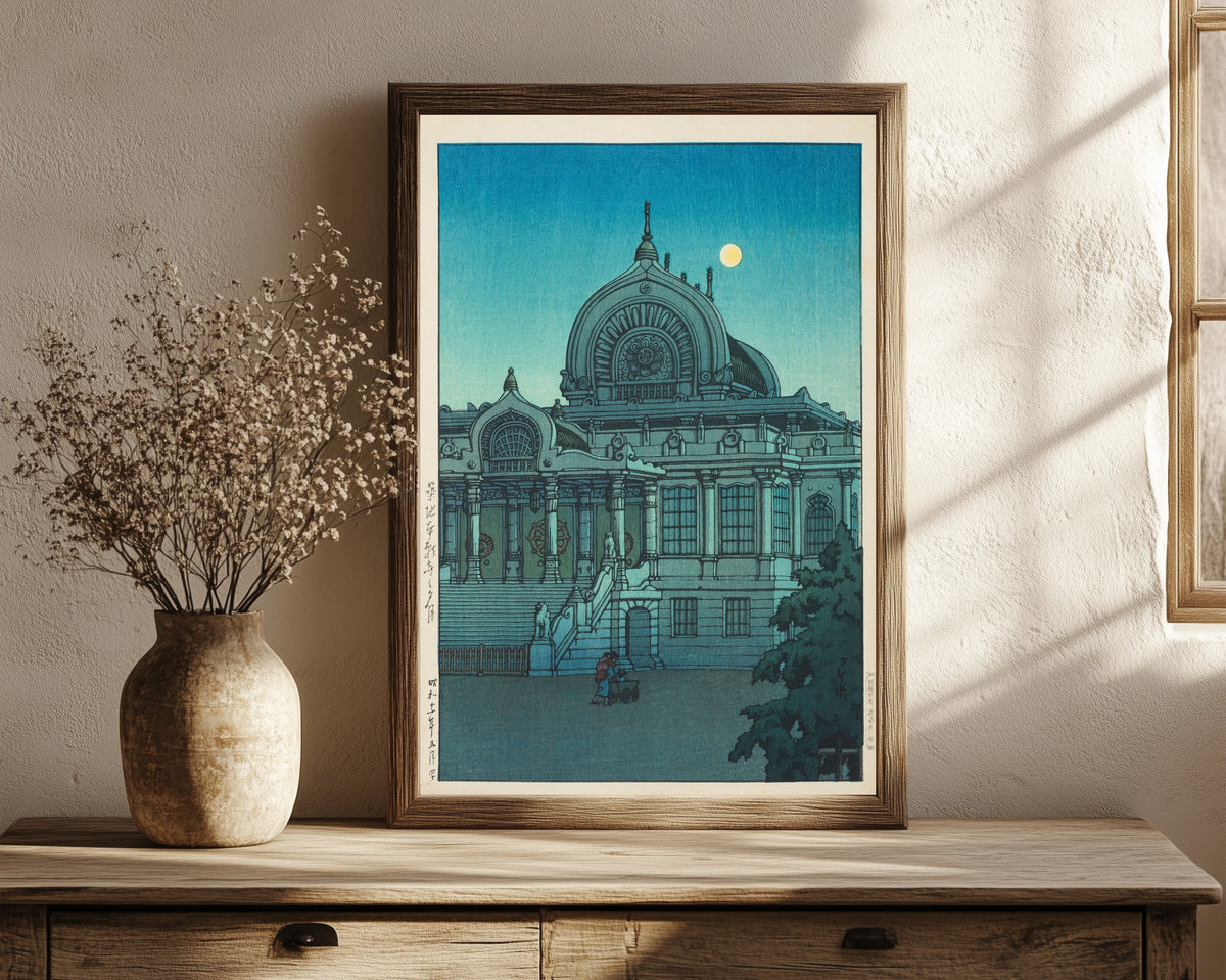 Framed art print of Evening Moon at Honganji Temple, Tsukiji by Kawase Hasui, in a dark wood frame leaning on a rustic console beside dried flowers