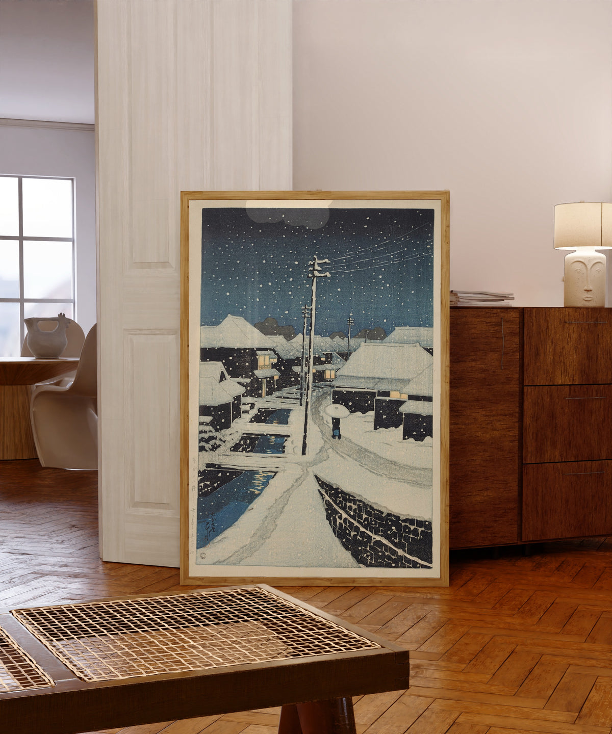 Framed art print of Evening Snow at Terajima Village by Kawase Hasui, in a light wood frame leaning in a warm room with a parquet floor