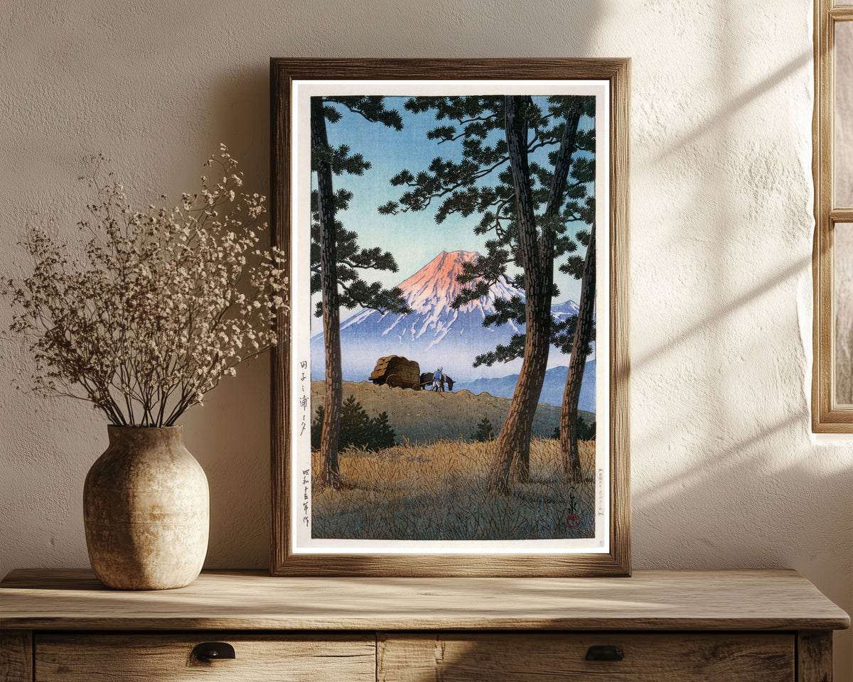 Framed art print of Fuji Mountain by Kawase Hasui, in a dark wood frame leaning on a rustic console beside dried flowers