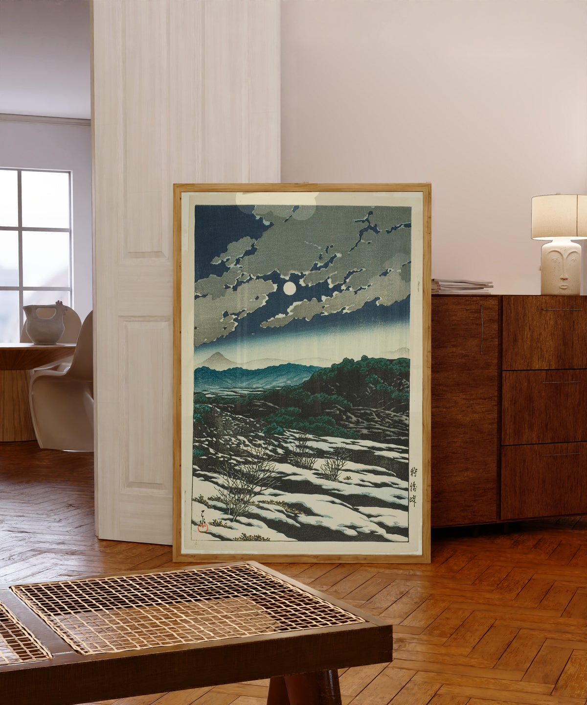 Framed art print of Karikachi Mountain Pass by Kawase Hasui, in a light wood frame leaning in a warm room with a parquet floor