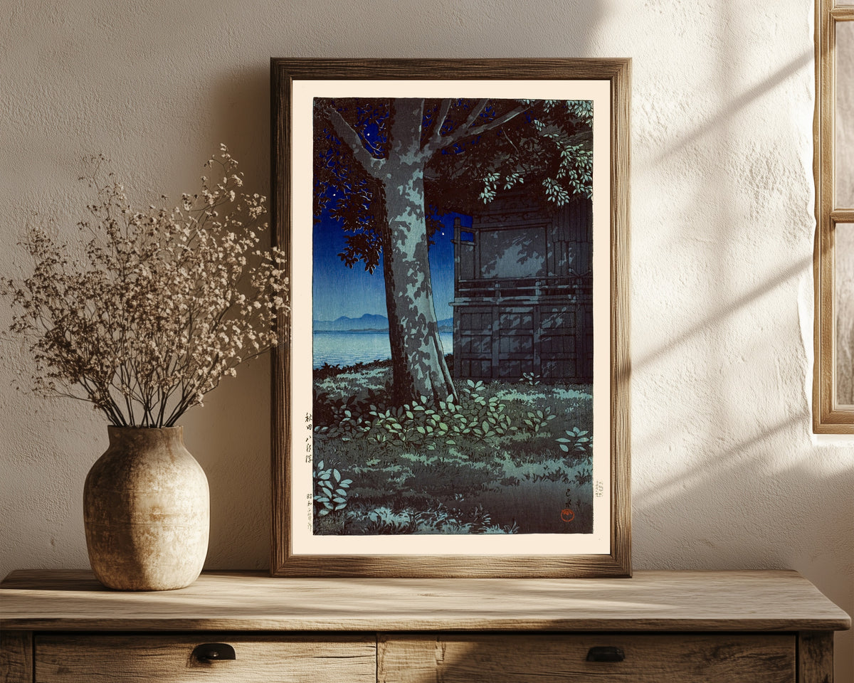 Framed art print of Lake Hachirogata at Night by Kawase Hasui, in a dark wood frame leaning on a rustic console beside dried flowers