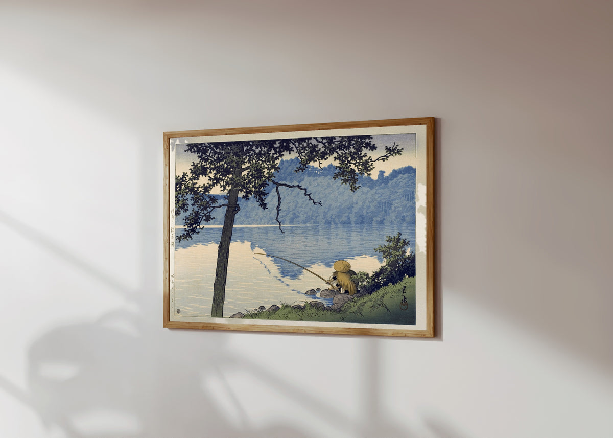 Framed art print of Lake Matsubara by Kawase Hasui, in a light wood frame on a sunlit white wall, seen at a slight angle