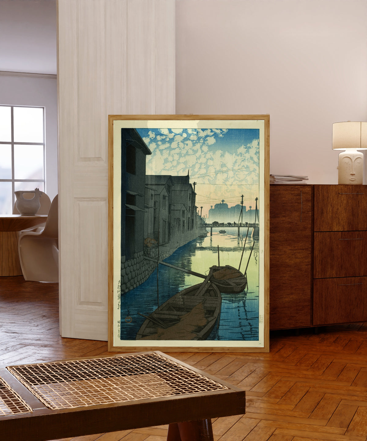 Framed art print of Morning at Daikon Wharf by Kawase Hasui, in a light wood frame leaning in a warm room with a parquet floor