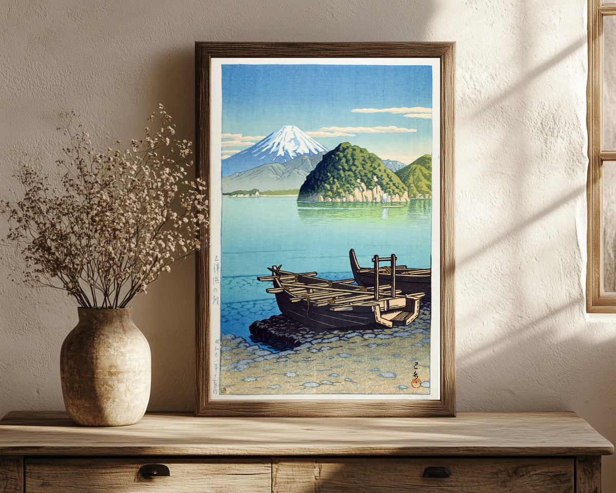 Framed art print of Morning at Miho Beach by Kawase Hasui, in a dark wood frame leaning on a rustic console beside dried flowers