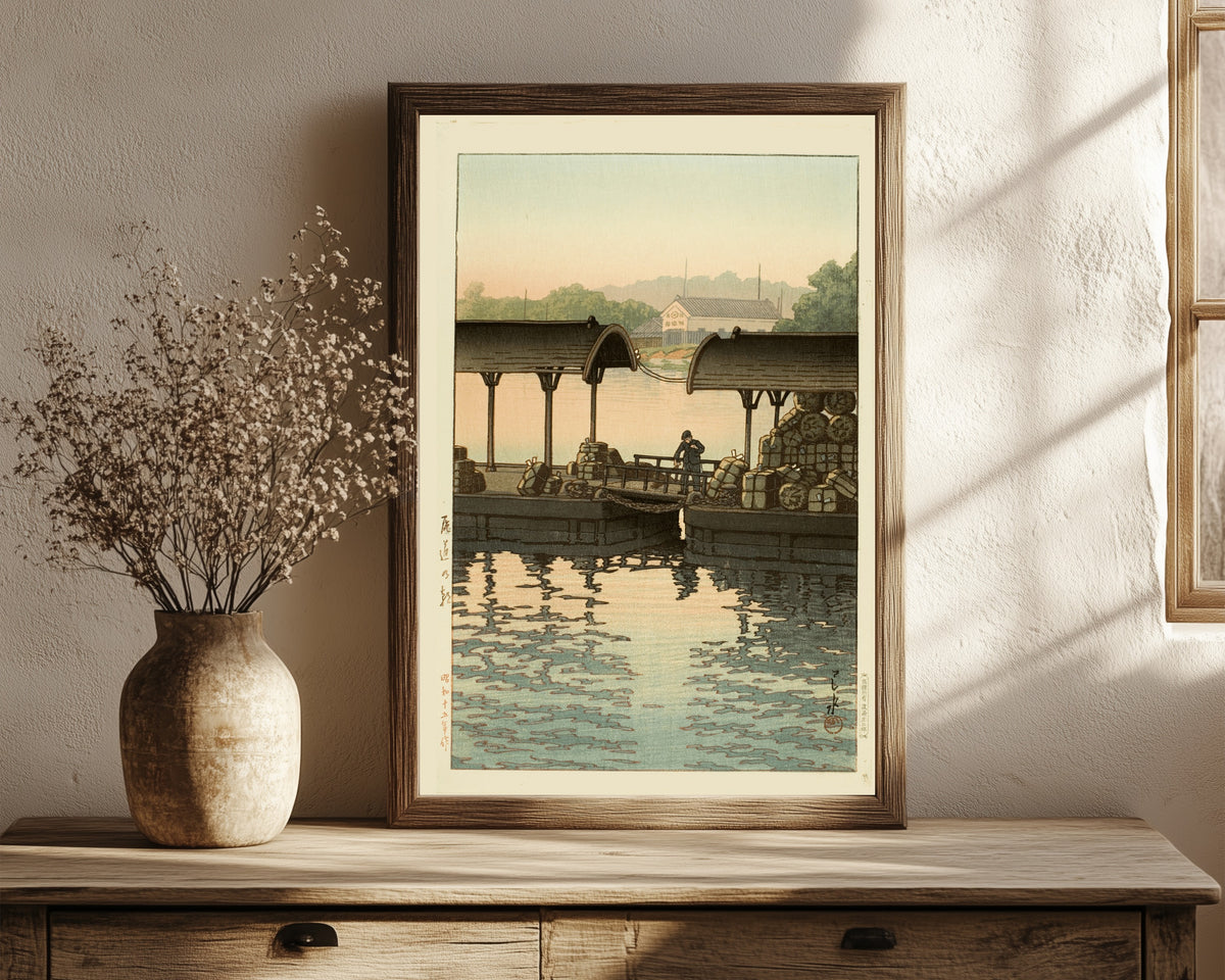Framed art print of Morning at Onomichi by Kawase Hasui, in a dark wood frame leaning on a rustic console beside dried flowers