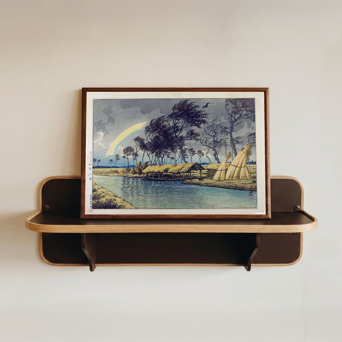 Framed art print of Rainbow at Hatta, Kaga Province by Kawase Hasui, in a dark wood frame resting on a wall shelf