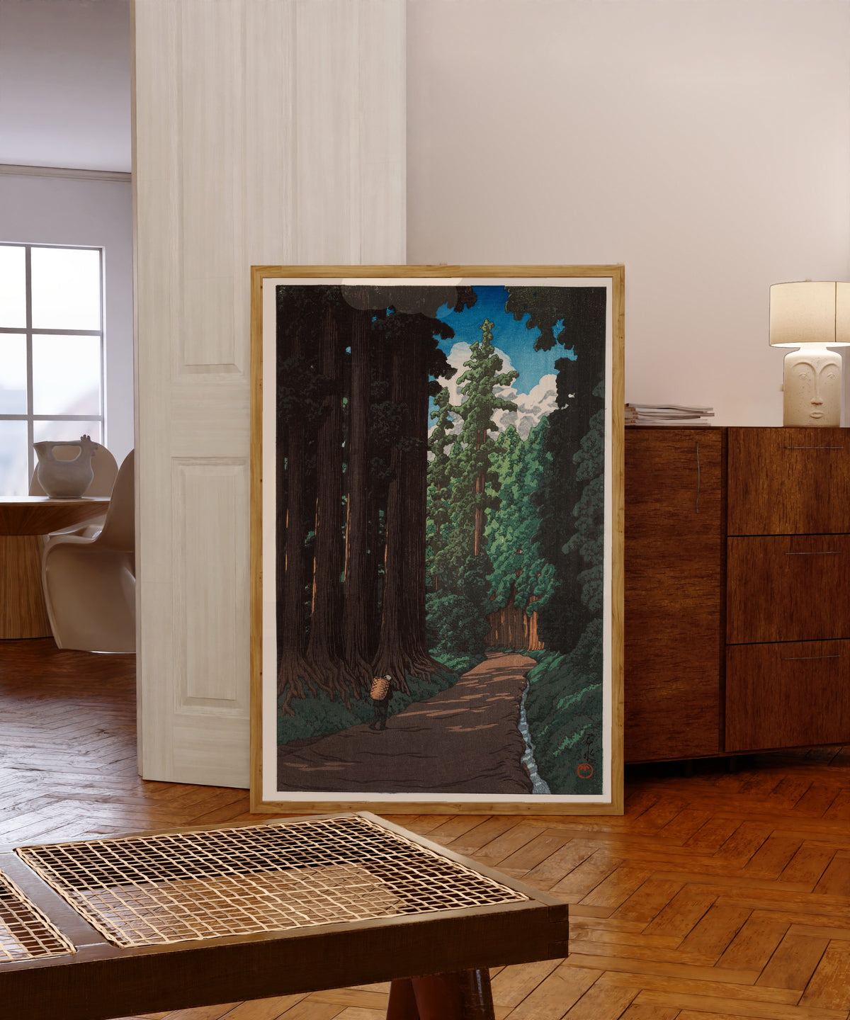 Framed art print of Road to Nikko by Kawase Hasui, in a light wood frame leaning in a warm room with a parquet floor