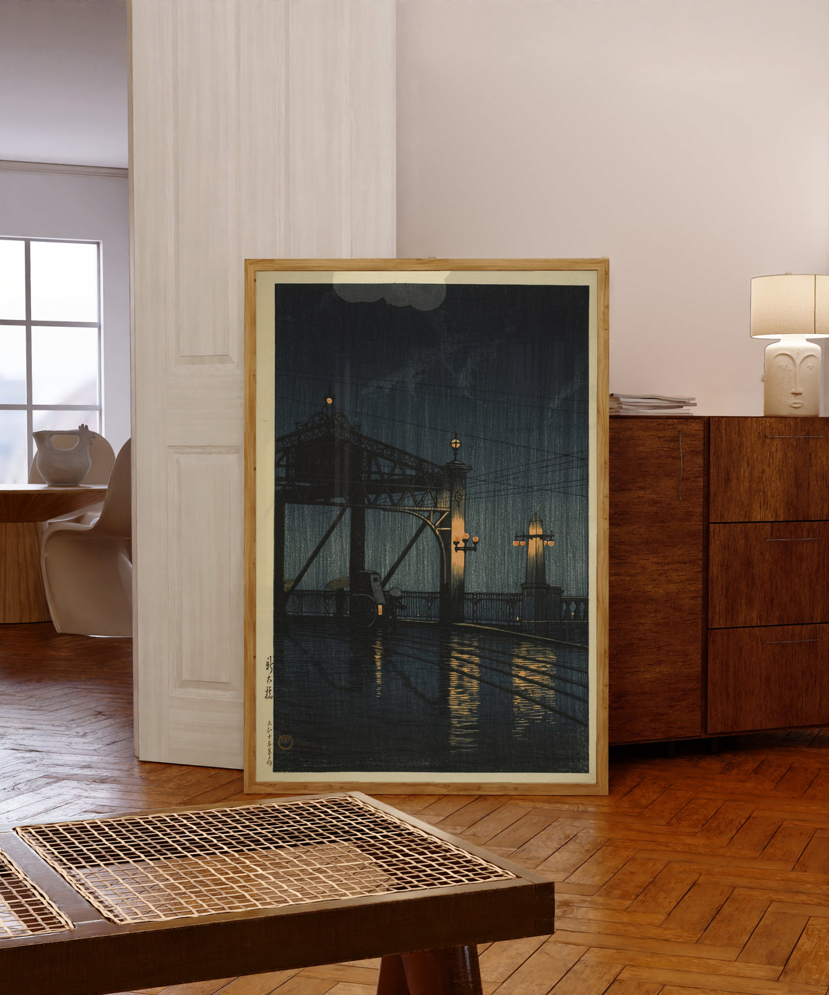 Framed art print of Shin Ohashi Bridge at Night by Kawase Hasui, in a light wood frame leaning in a warm room with a parquet floor