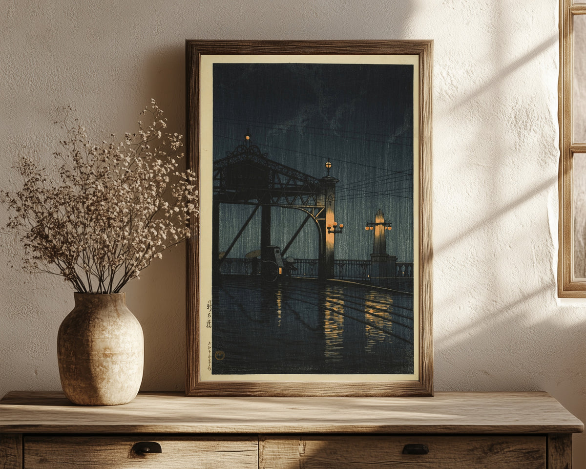 Framed art print of Shin Ohashi Bridge at Night by Kawase Hasui, in a dark wood frame leaning on a rustic console beside dried flowers