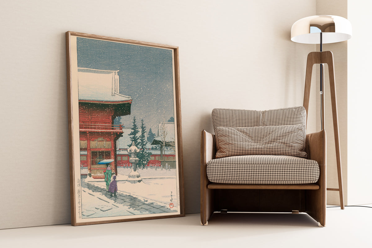 Framed art print of Snow at Nezu Gongen Shrine by Kawase Hasui, leaning against a wall beside an armchair and a floor lamp