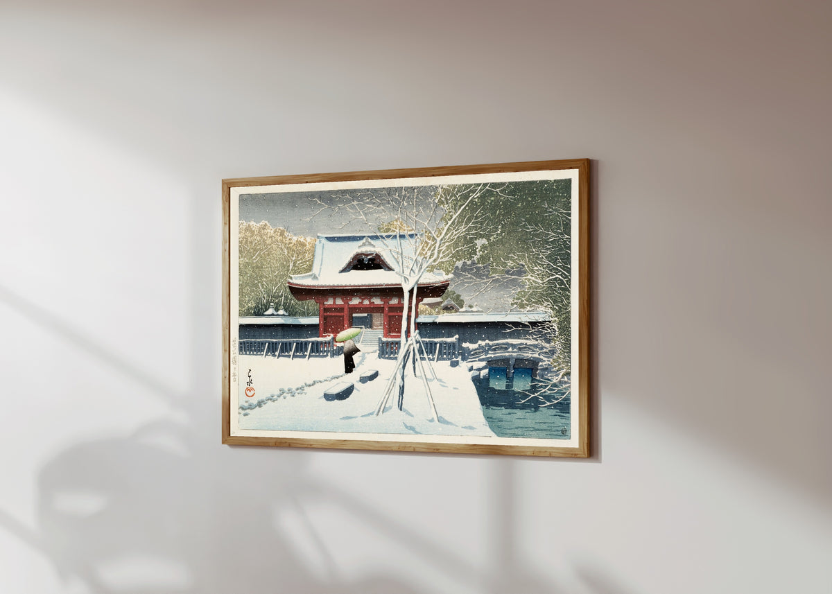Framed art print of Snow at Shiba Park by Kawase Hasui, in a light wood frame on a sunlit white wall, seen at a slight angle