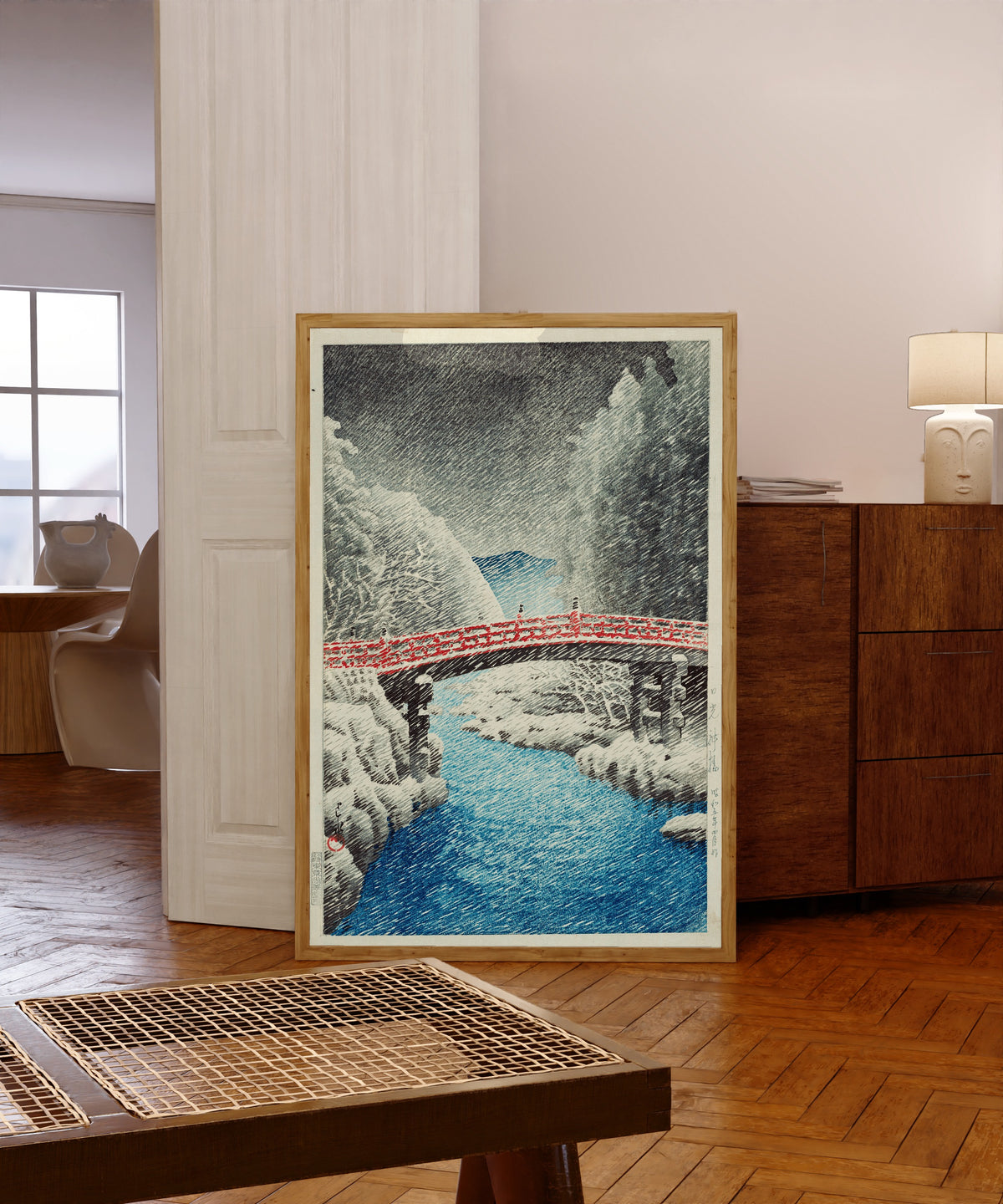 Framed art print of Snow at Shinkyo Bridge, Nikko by Kawase Hasui, in a light wood frame leaning in a warm room with a parquet floor