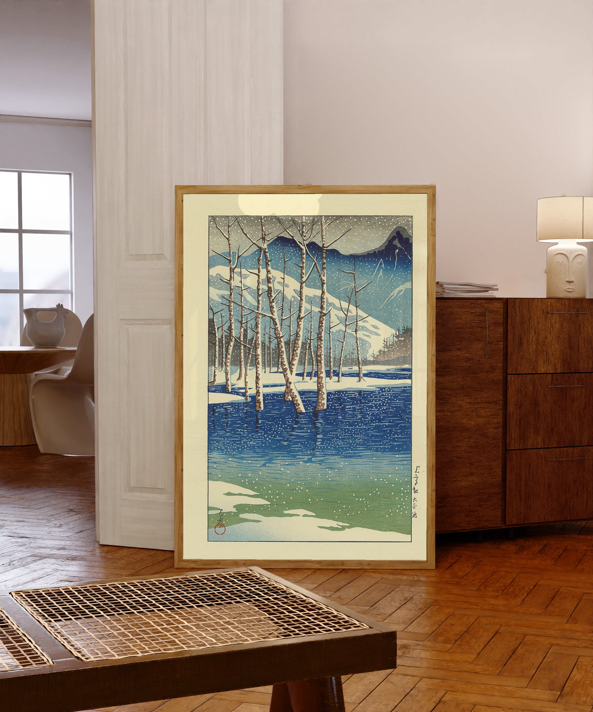 Framed art print of Taisho Pond by Kawase Hasui, in a light wood frame leaning in a warm room with a parquet floor