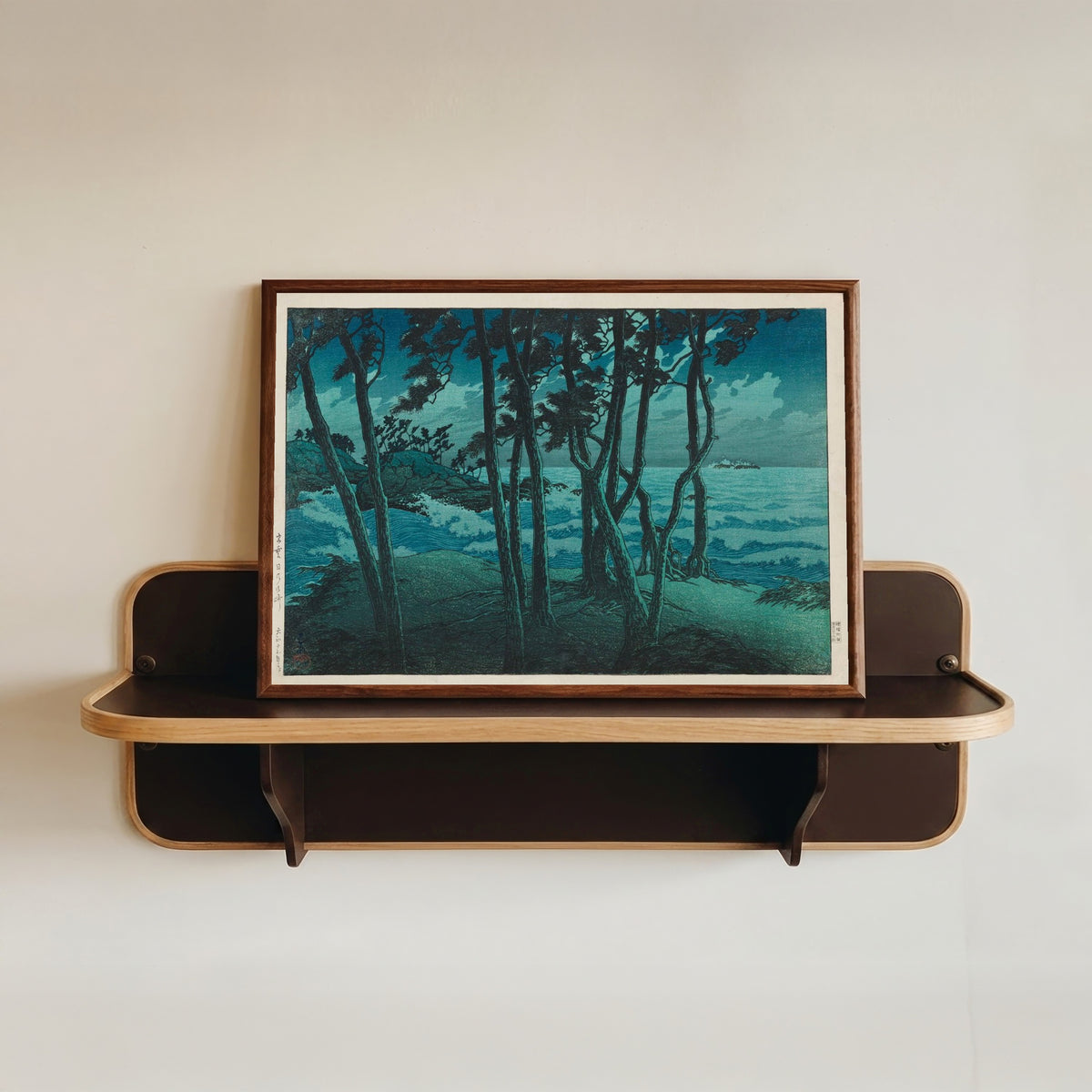 Framed art print of Izumo Seafront by Kawase Hasui, in a dark wood frame resting on a wall shelf