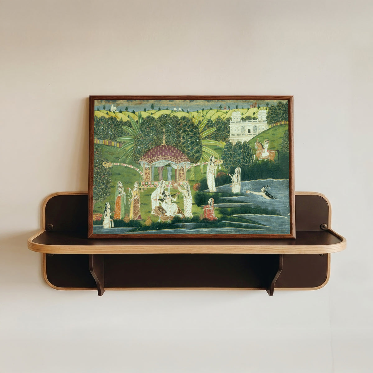 Framed art print of Bani Thani Bathing at Pholl Sagar Palace by Kishangarh school, in a dark wood frame resting on a wall shelf