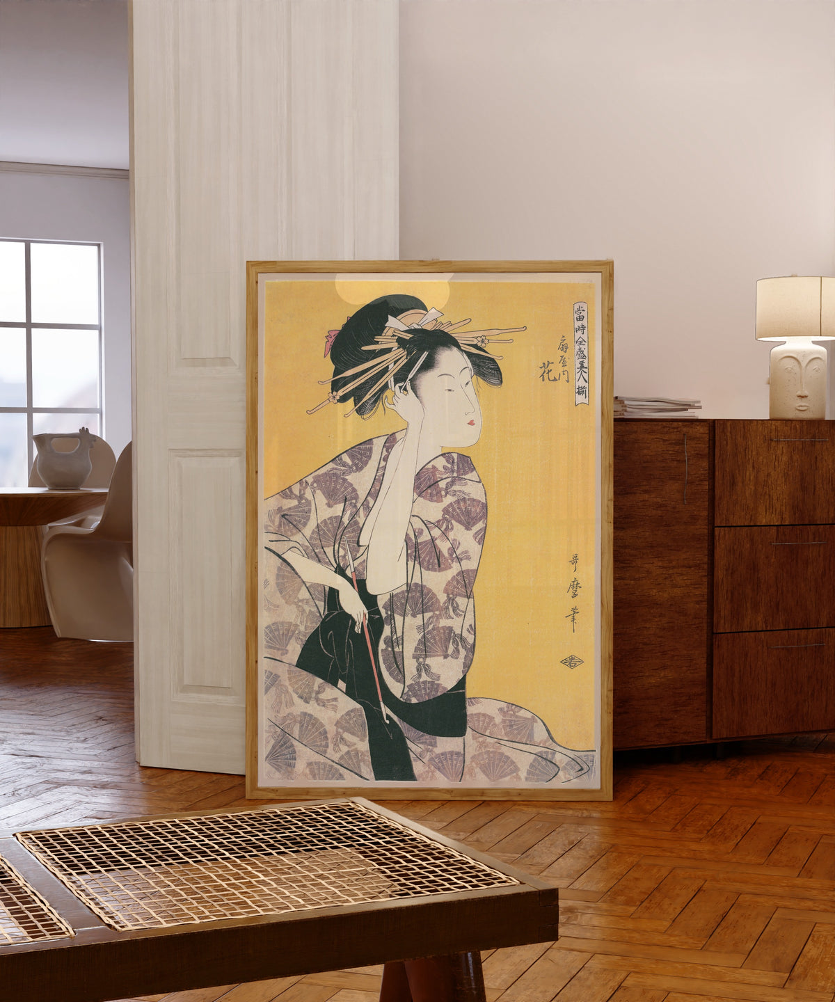 Framed art print of Hanaogi of the Ogiya (Holding a Pipe) by Kitagawa Utamaro, in a light wood frame leaning in a warm room with a parquet floor