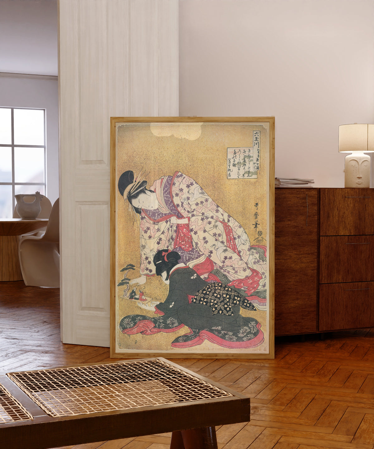 Framed art print of Seyama of the Matsubaya, kamuro Iroka and Yukari… by Kitagawa Utamaro, in a light wood frame leaning in a warm room with a parquet floor