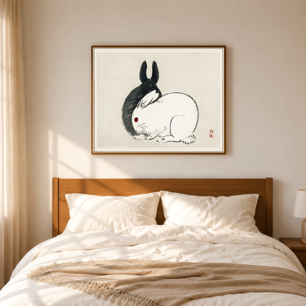 Framed art print of Black and White Rabbits by Kōno Bairei, in a slim wood frame above a bed in a sunlit bedroom