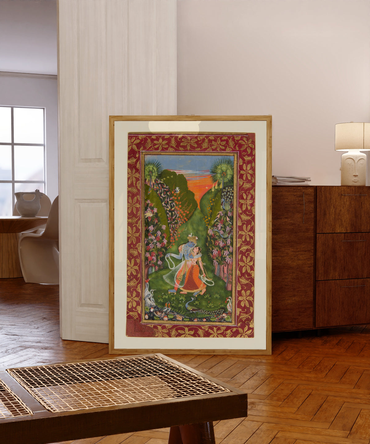 Framed art print of Radha and Krishna Walk in a Flowering Grove by Kota school, in a light wood frame leaning in a warm room with a parquet floor