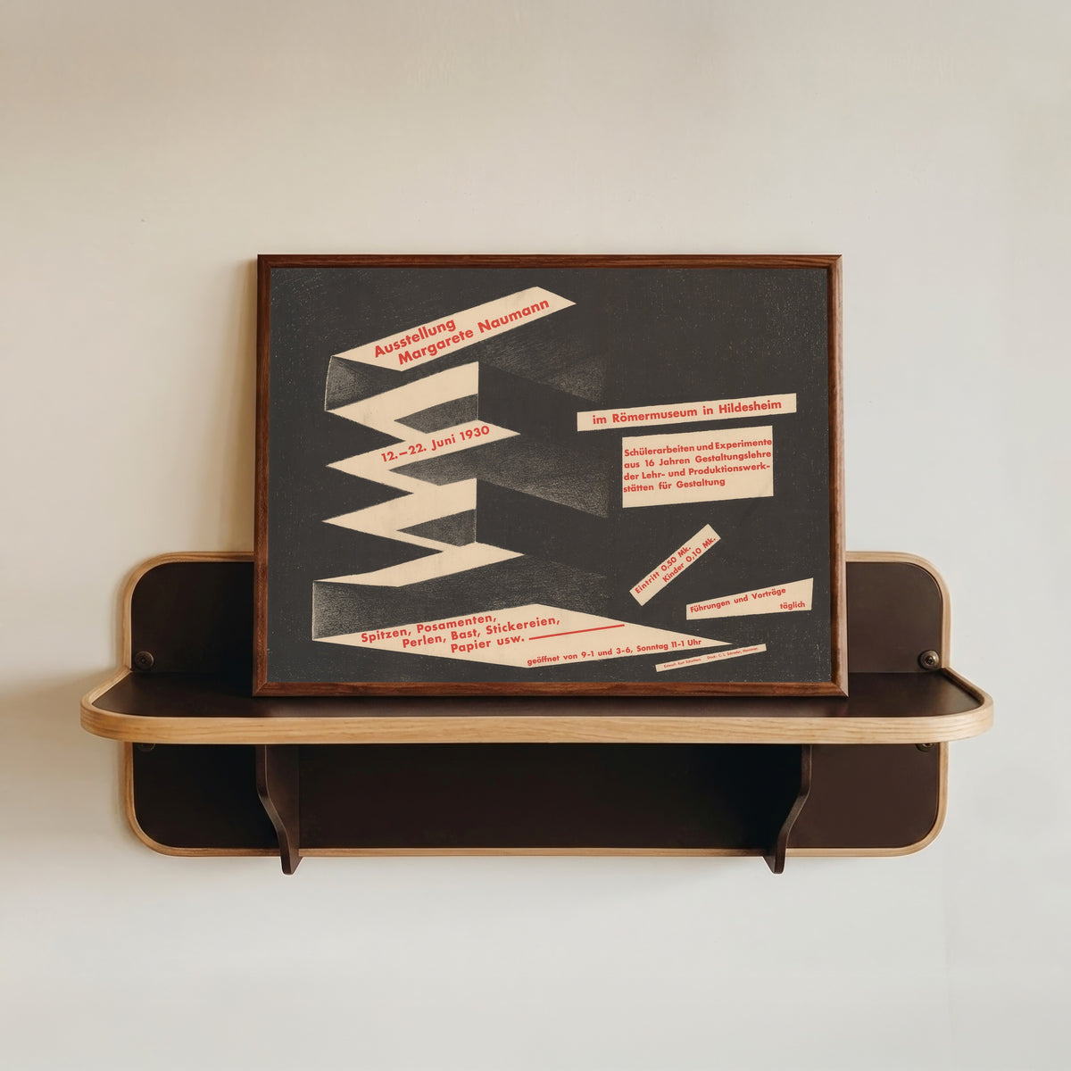 Framed art print of Ausstellung Margarete Naumann, Römermuseum Hildesheim by Kurt Schwitters, in a dark wood frame resting on a wall shelf