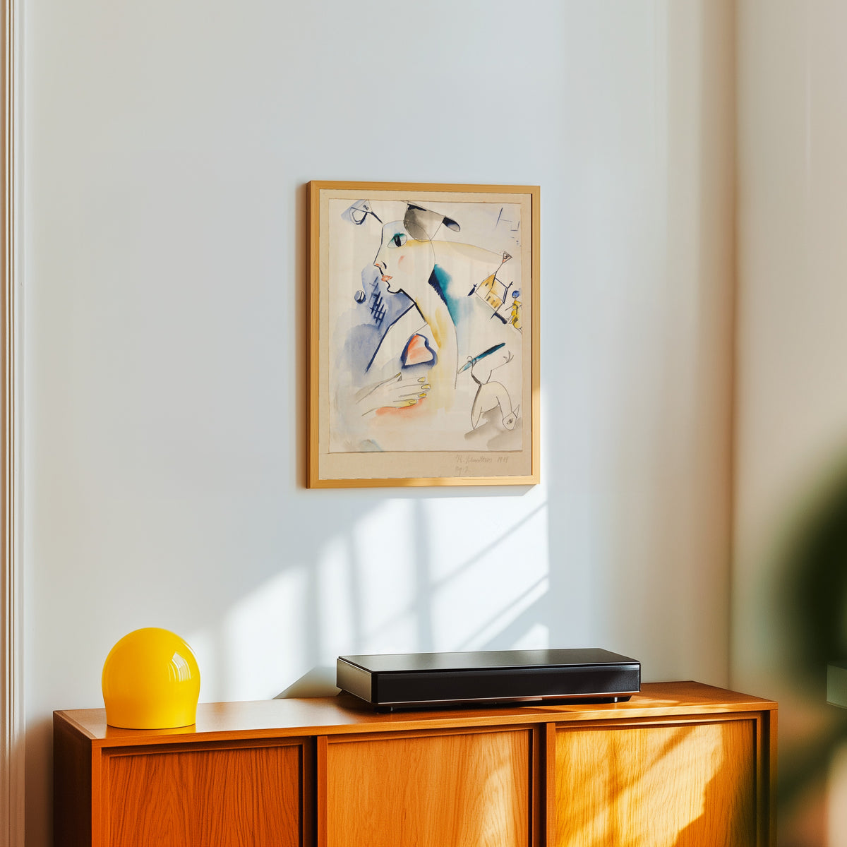 Framed art print of Mann schaaft Lilablau by Kurt Schwitters, in a light wood frame on a white wall above an orange sideboard