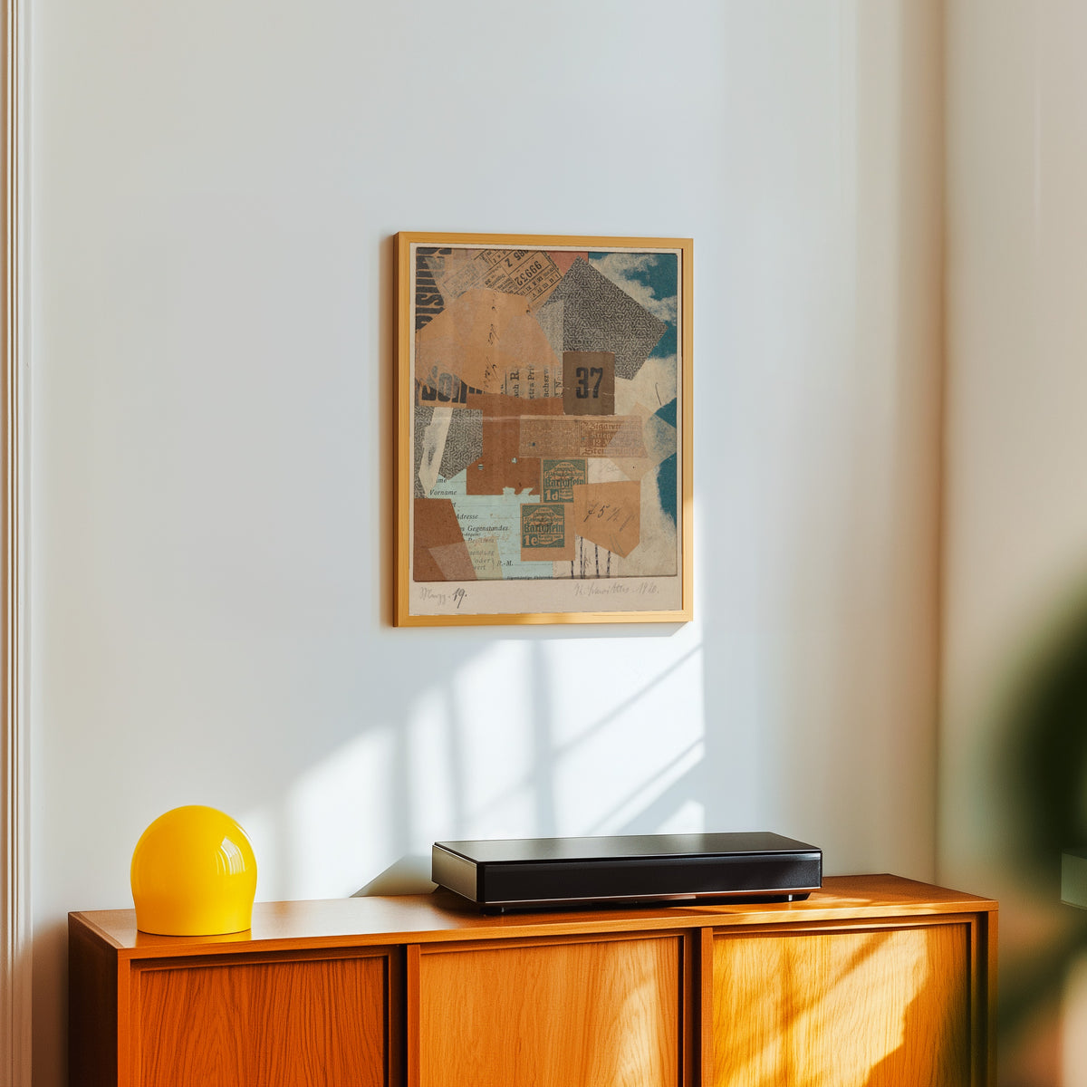 Framed art print of Merzz. 19 by Kurt Schwitters, in a light wood frame on a white wall above an orange sideboard