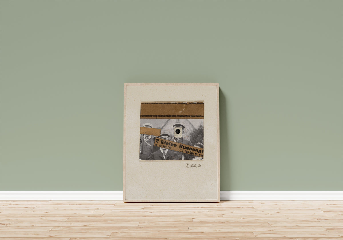 Framed art print of Ohne titel (2 kleine Russenpf) by Kurt Schwitters, in a light wood frame leaning on a sage green wall above a wooden floor