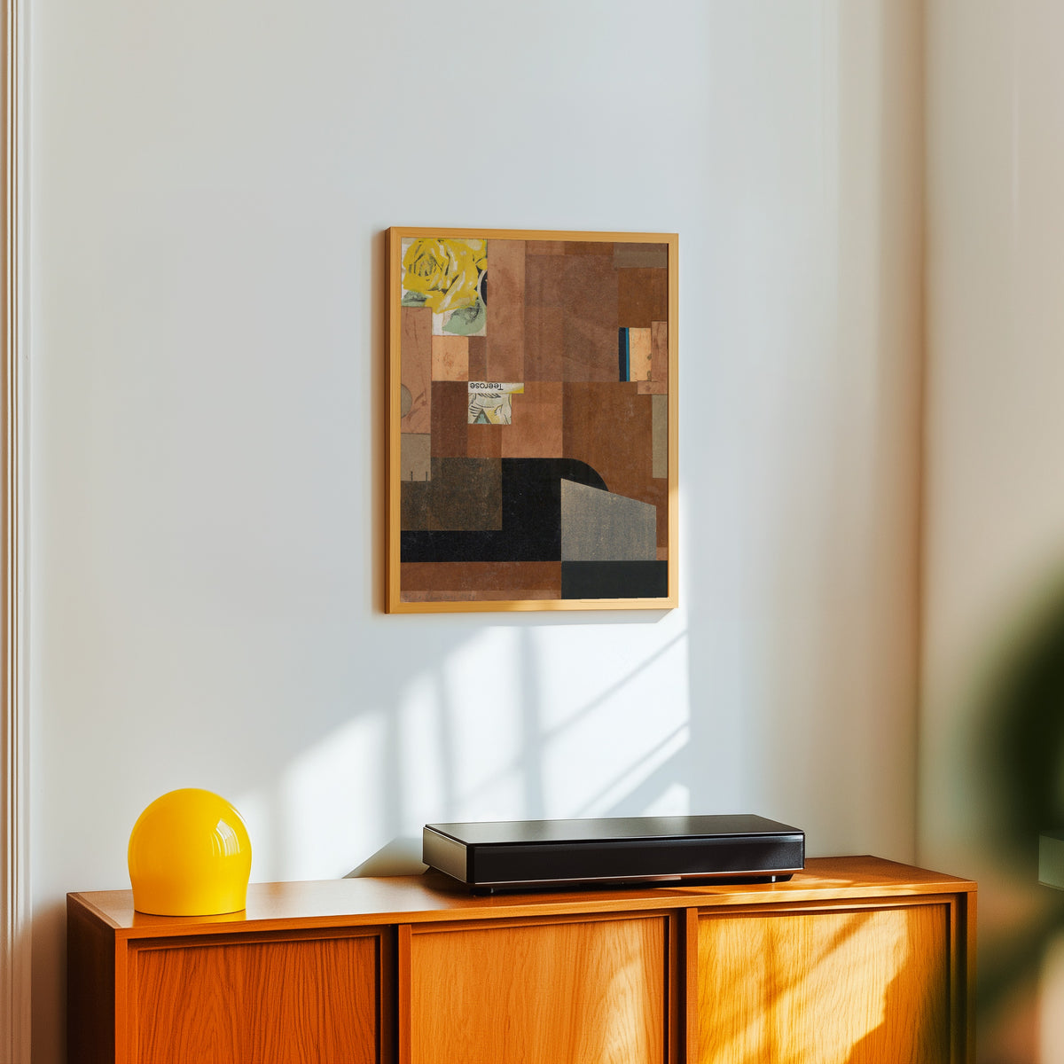 Framed art print of Tea Rose by Kurt Schwitters, in a light wood frame on a white wall above an orange sideboard