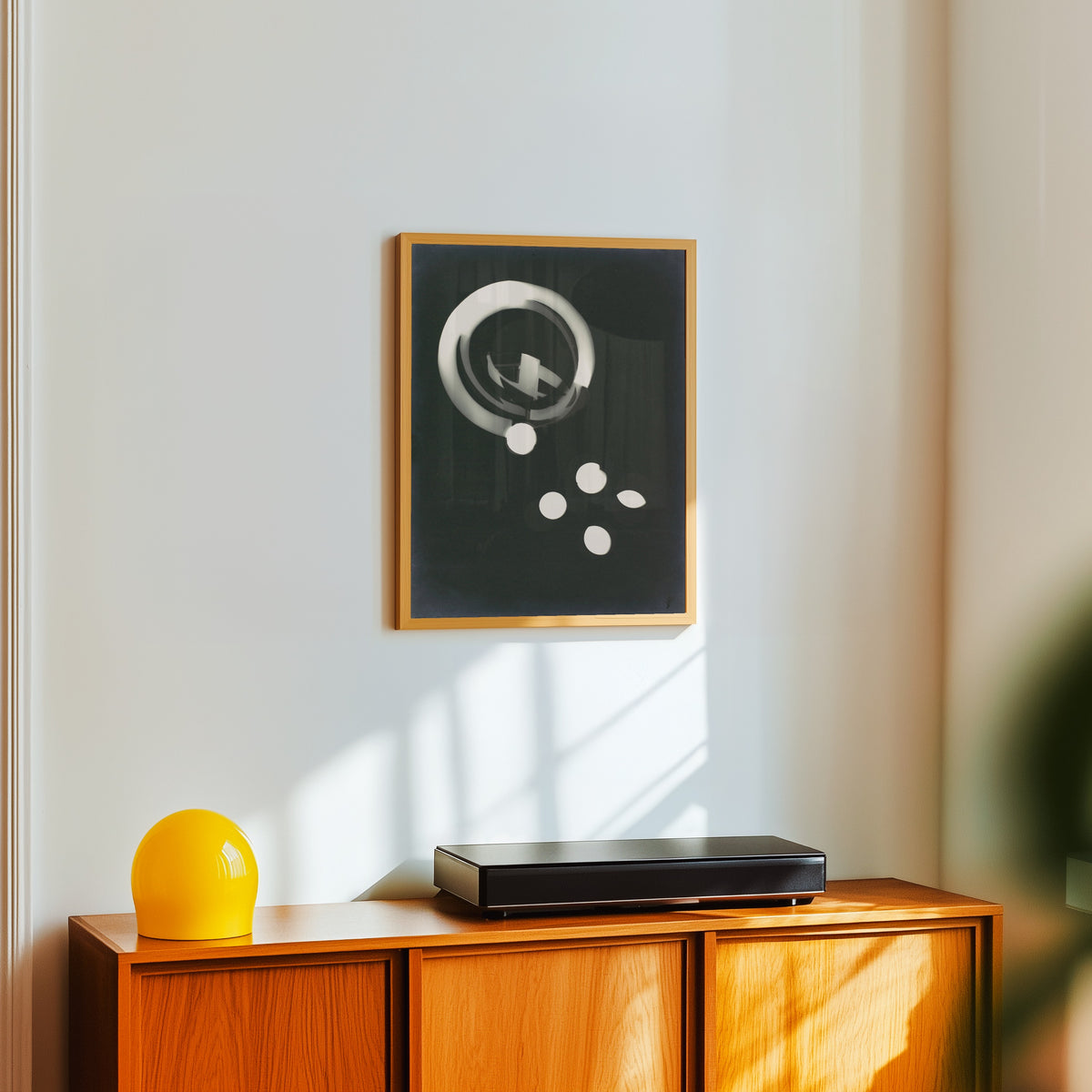 Framed art print of Fotogramm (1925) by László Moholy-Nagy, in a light wood frame on a white wall above an orange sideboard