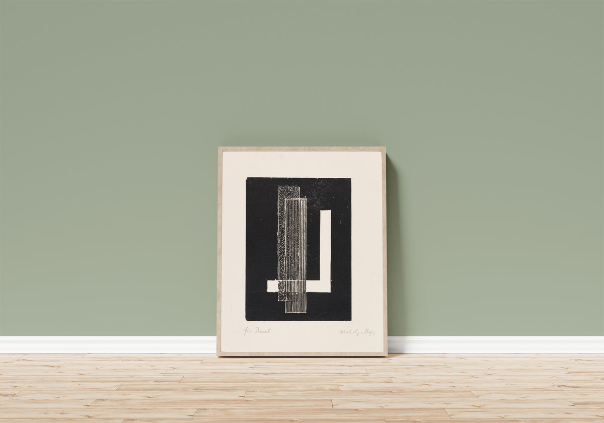 Framed art print of Ohne Titel by László Moholy-Nagy, in a light wood frame leaning on a sage green wall above a wooden floor