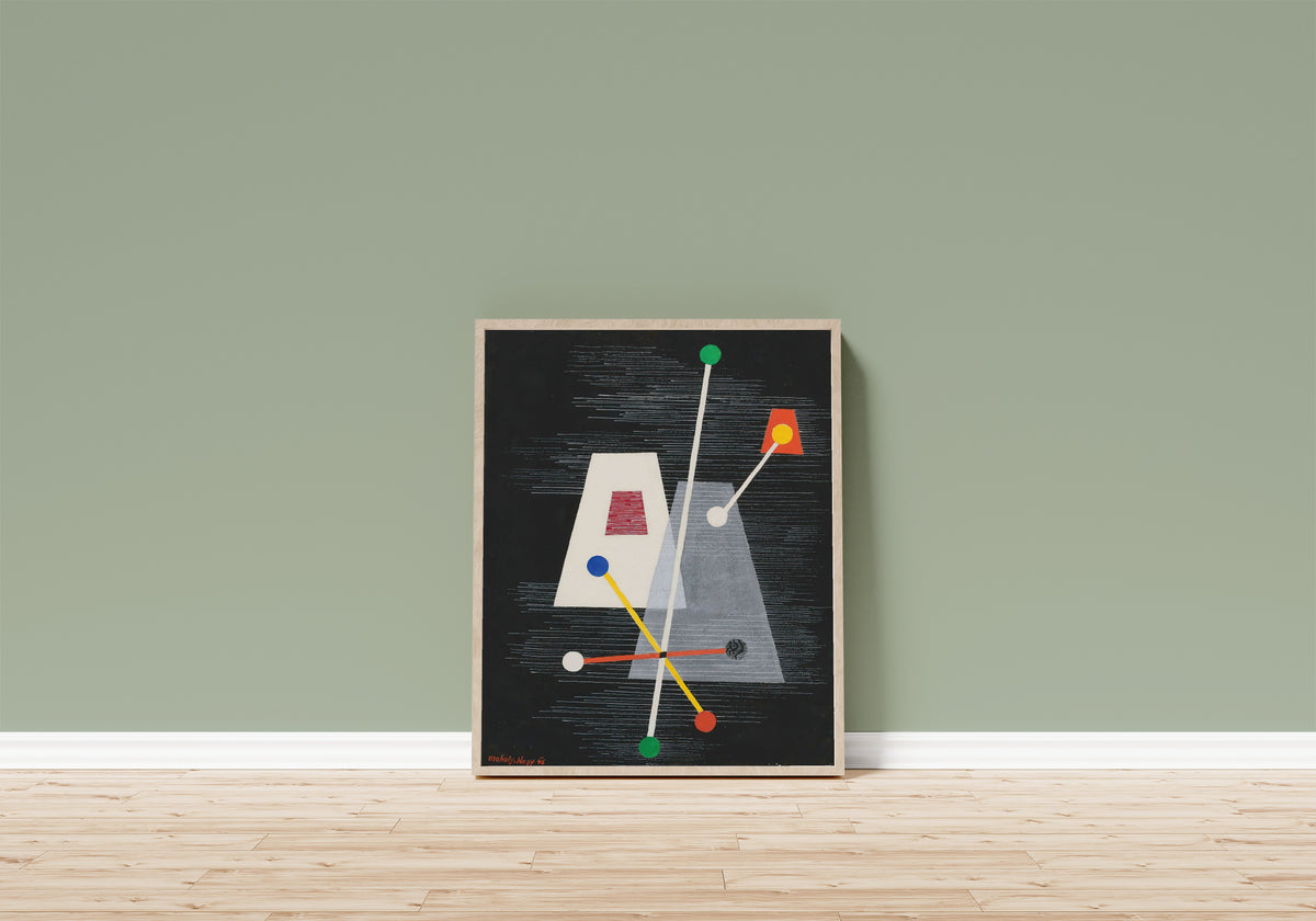 Framed art print of Truncated Pyramids by László Moholy-Nagy, in a light wood frame leaning on a sage green wall above a wooden floor
