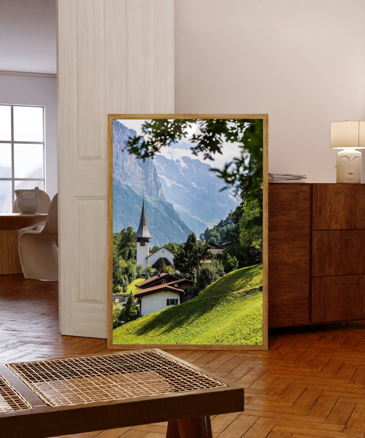 Framed art print of Lauterbrunnen by Daniela Faust, in a light wood frame leaning in a warm room with a parquet floor