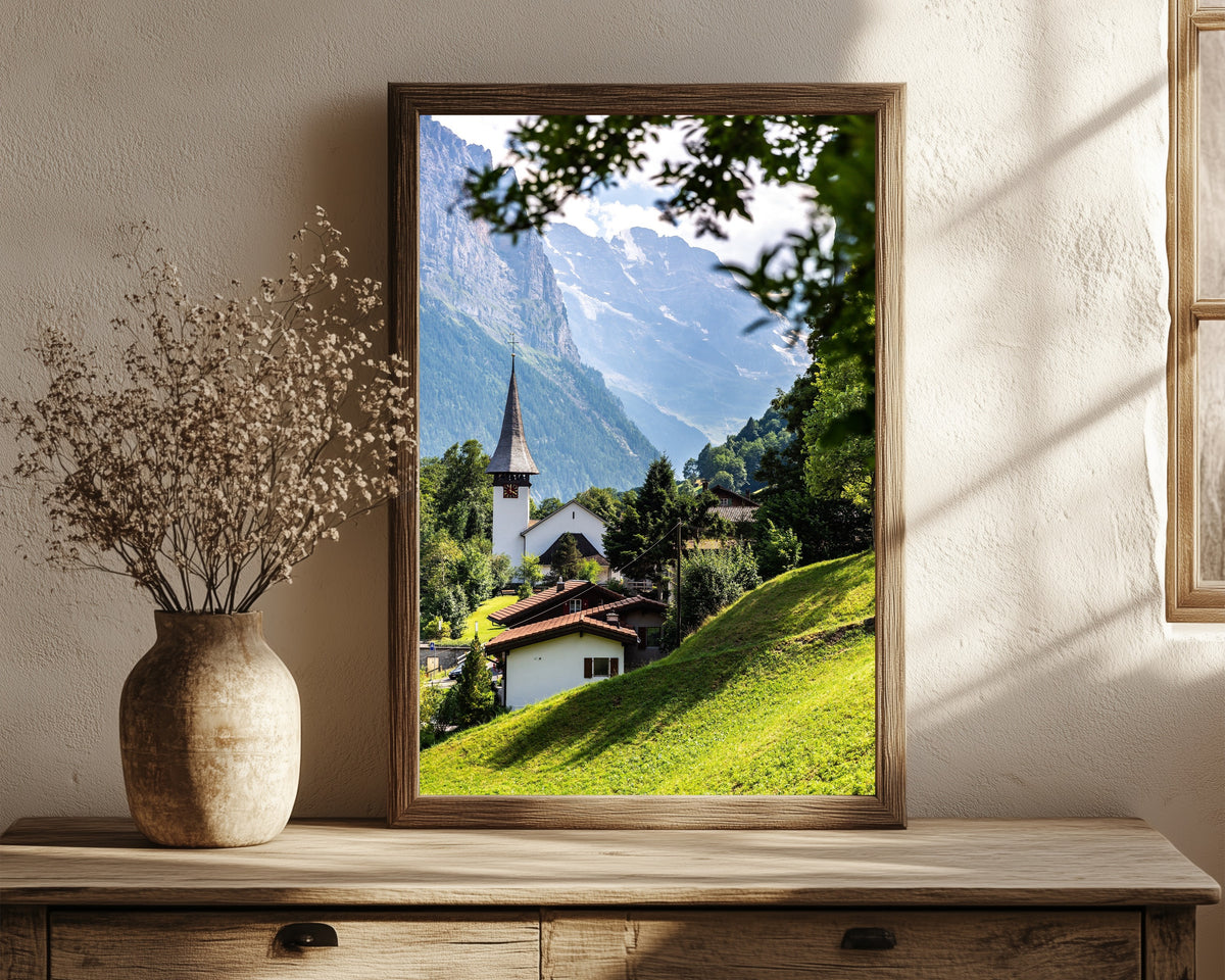 Framed art print of Lauterbrunnen by Daniela Faust, in a dark wood frame leaning on a rustic console beside dried flowers
