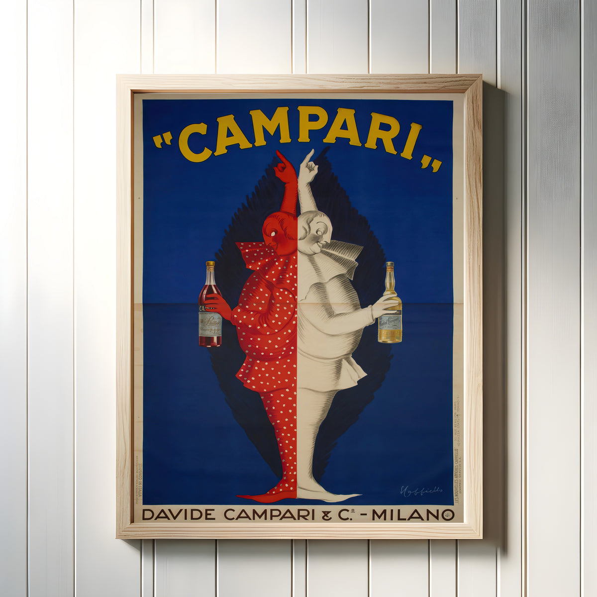 Framed art print of Campari by Leonetto Cappiello, in a light wood frame on a white panelled wall