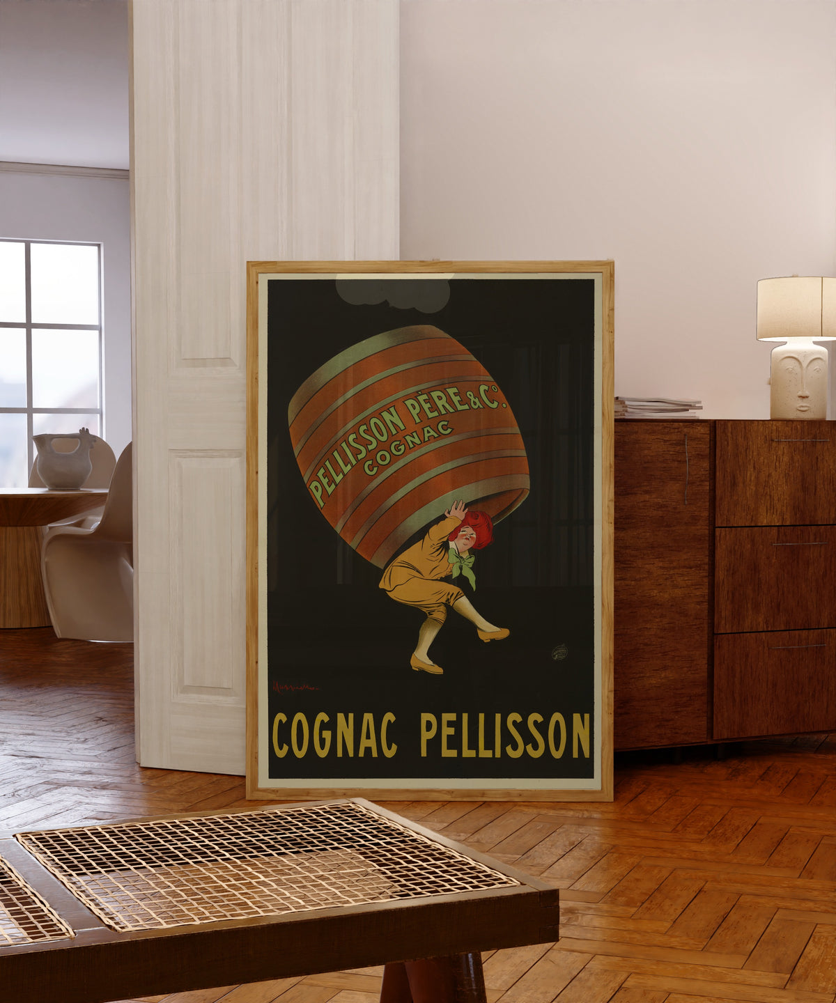Framed art print of Pellisson père et Cie Cognac by Leonetto Cappiello, in a light wood frame leaning in a warm room with a parquet floor