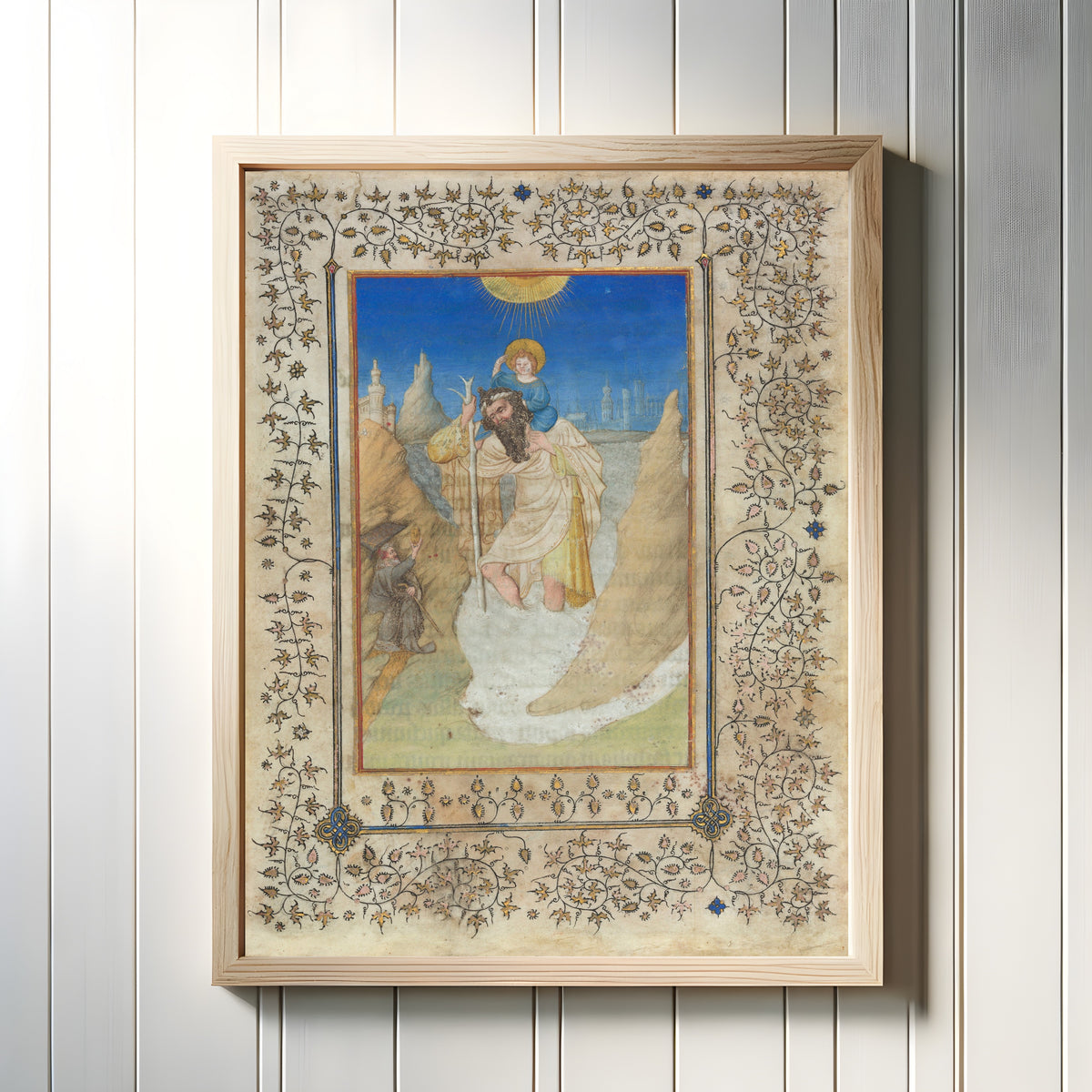 Framed art print of Saint Christopher Carrying the Christ Child by Limbourg Brothers, in a light wood frame on a white panelled wall