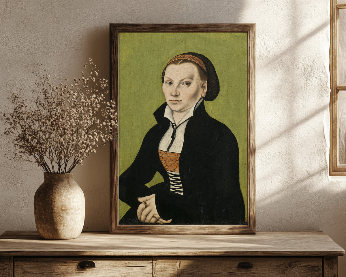 Framed art print of Katharina von Bora, Wife of Martin Luther by Lucas Cranach the Elder, in a dark wood frame leaning on a rustic console beside dried flowers