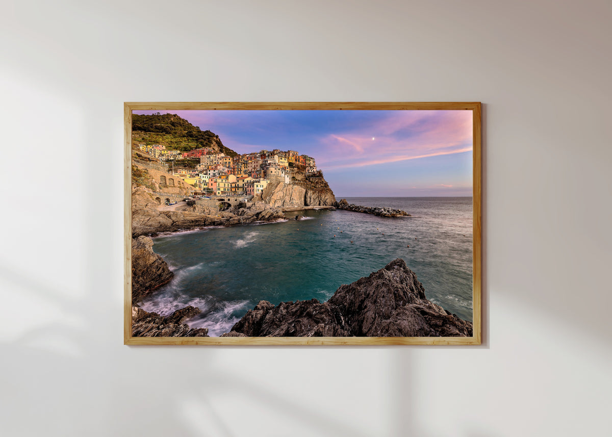 Framed art print of Manarola Sunset by Pablo Meilán Campagnale, in a light wood frame on a sunlit white wall