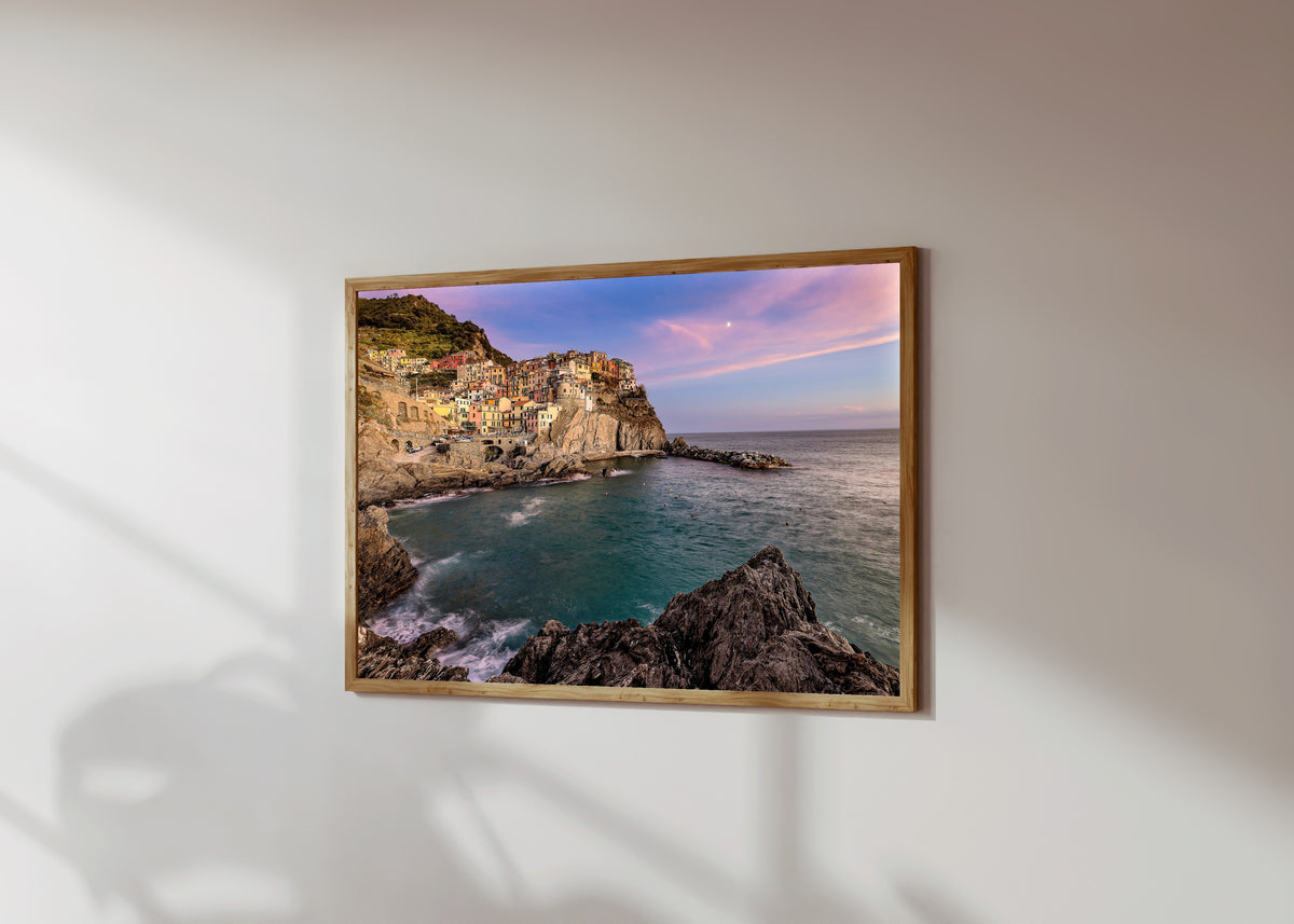 Framed art print of Manarola Sunset by Pablo Meilán Campagnale, in a light wood frame on a sunlit white wall, seen at a slight angle