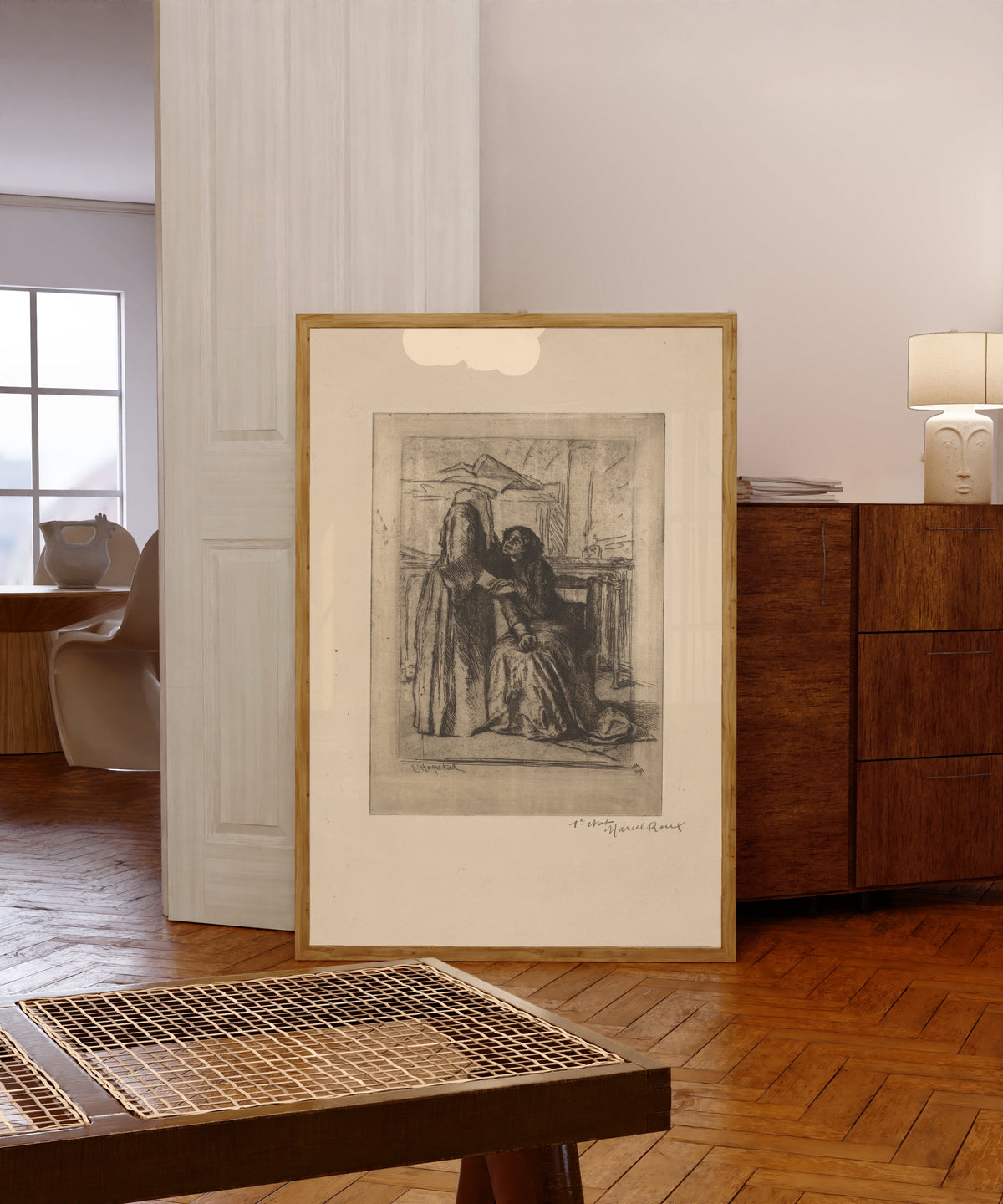 Framed art print of The Hospital (1904) by Marcel Roux, in a light wood frame leaning in a warm room with a parquet floor