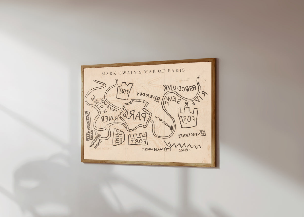 Framed art print of Mark Twain's Map of Paris by Mark Twain, in a light wood frame on a sunlit white wall, seen at a slight angle