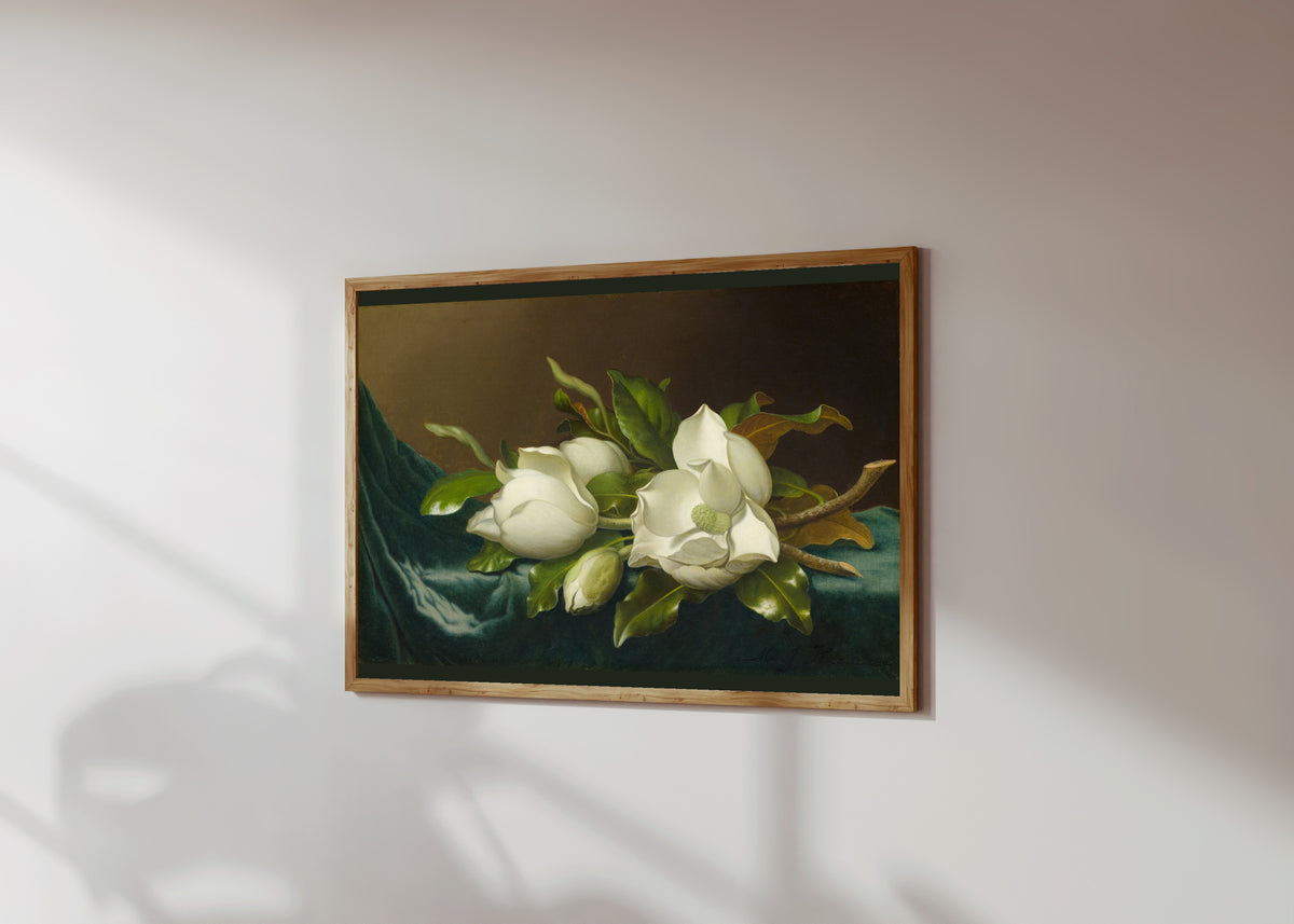 Framed art print of Magnolias on Light Blue Velvet Cloth by Martin Johnson Heade, in a light wood frame on a sunlit white wall, seen at a slight angle