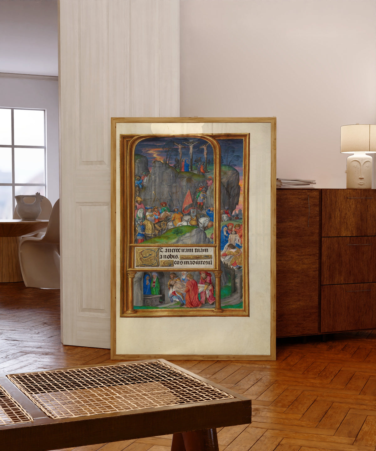 Framed art print of Spinola Hours: The Crucifixion by Master of James IV of Scotland, in a light wood frame leaning in a warm room with a parquet floor