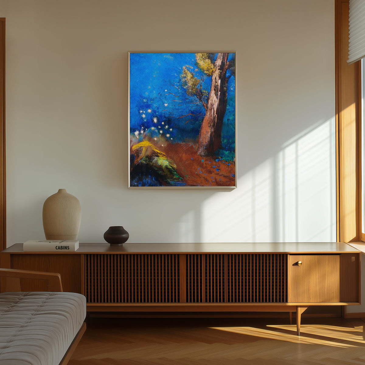 Framed art print of The Death of Buddha by Odilon Redon, in a thin light frame on a sunlit wall above a wooden sideboard
