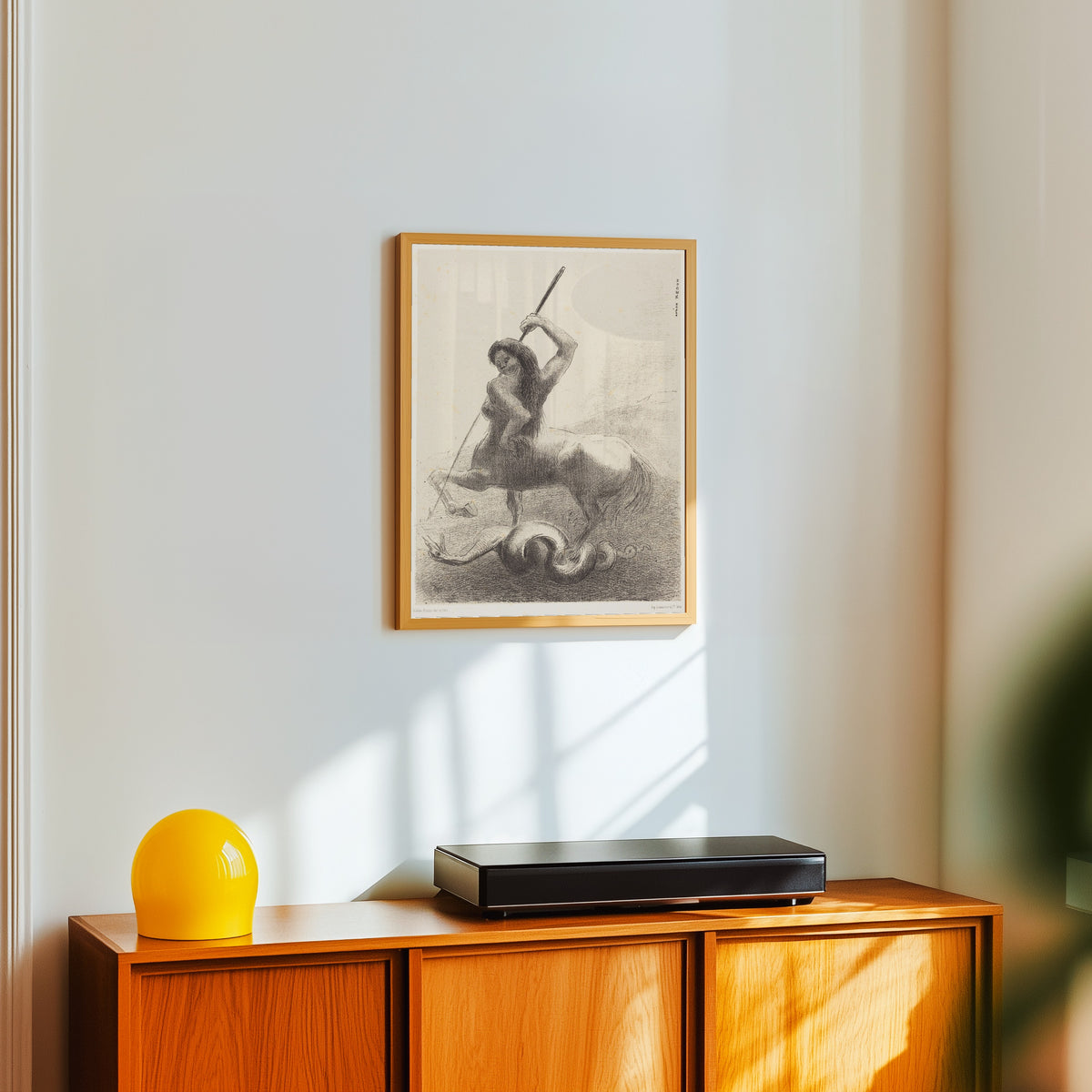 Framed art print of The Origins: There Were Struggles and Vain Victories by Odilon Redon, in a light wood frame on a white wall above an orange sideboard