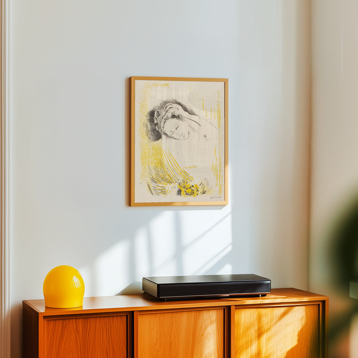 Framed art print of The Shulamite by Odilon Redon, in a light wood frame on a white wall above an orange sideboard