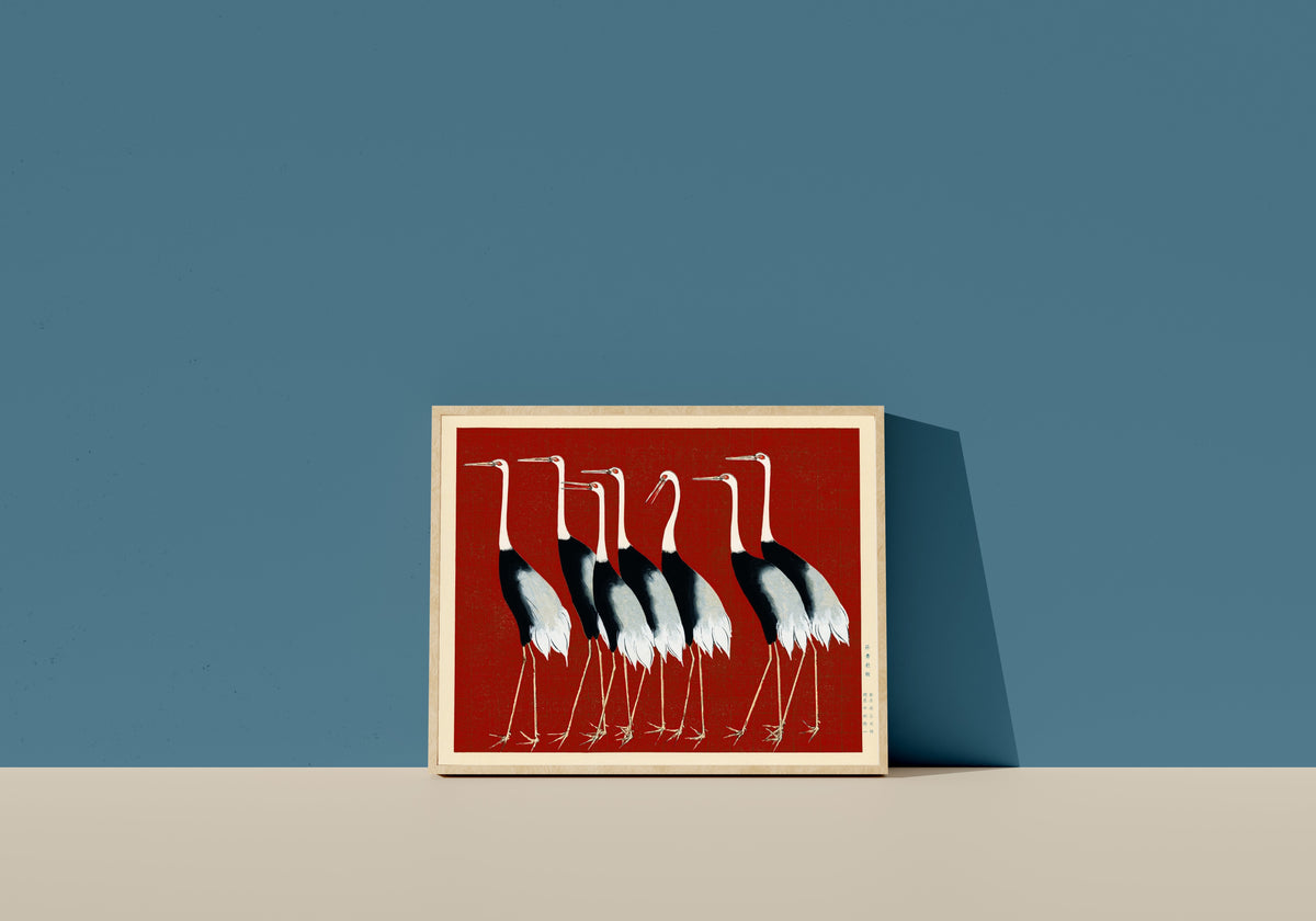 Framed art print of Cranes in Red by Ogata Korin, in a light wood frame leaning on a blue wall