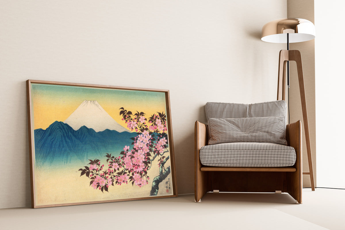 Cherry Blossoms and Mount Fuji by Ohara Koson — framed and leaning against a wall beside an armchair and a floor lamp
